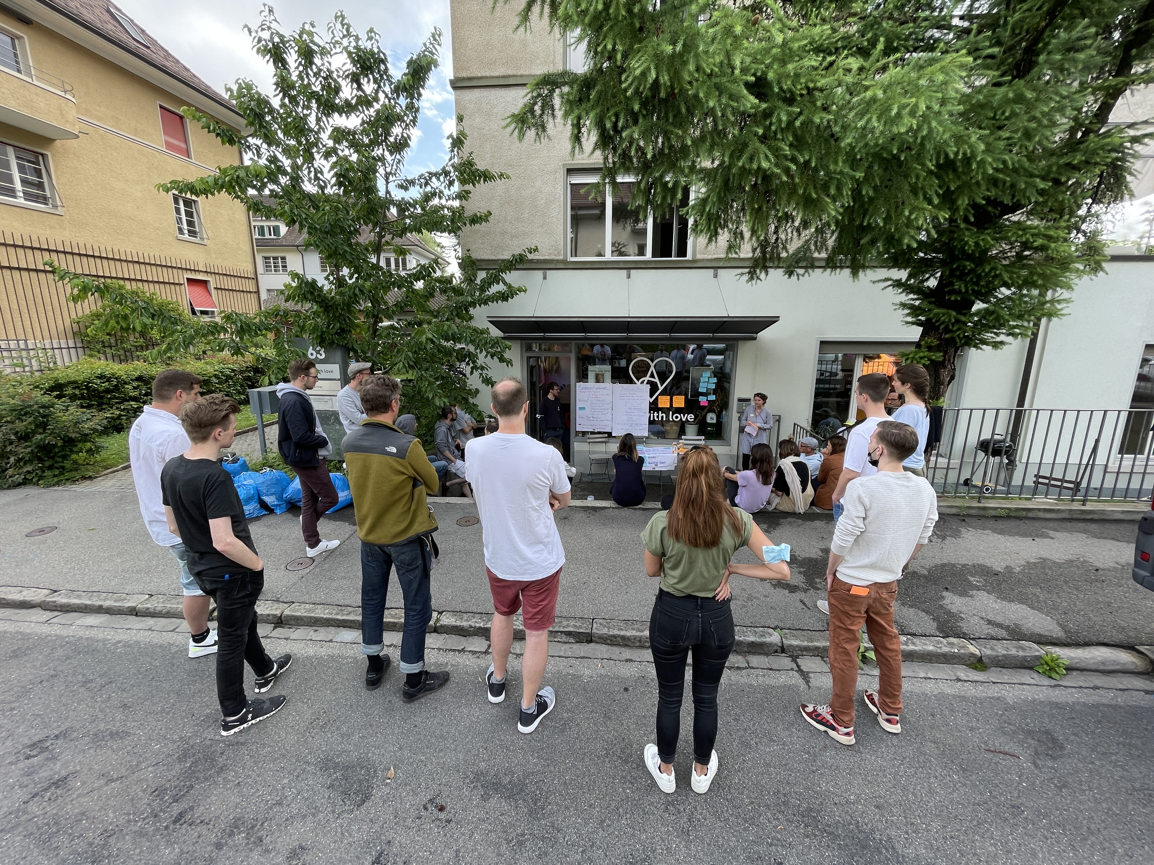 Mitarbeitende stehen verteilt vor dem Apps with love Büro und hören zu wie jemand etwas präsentiert