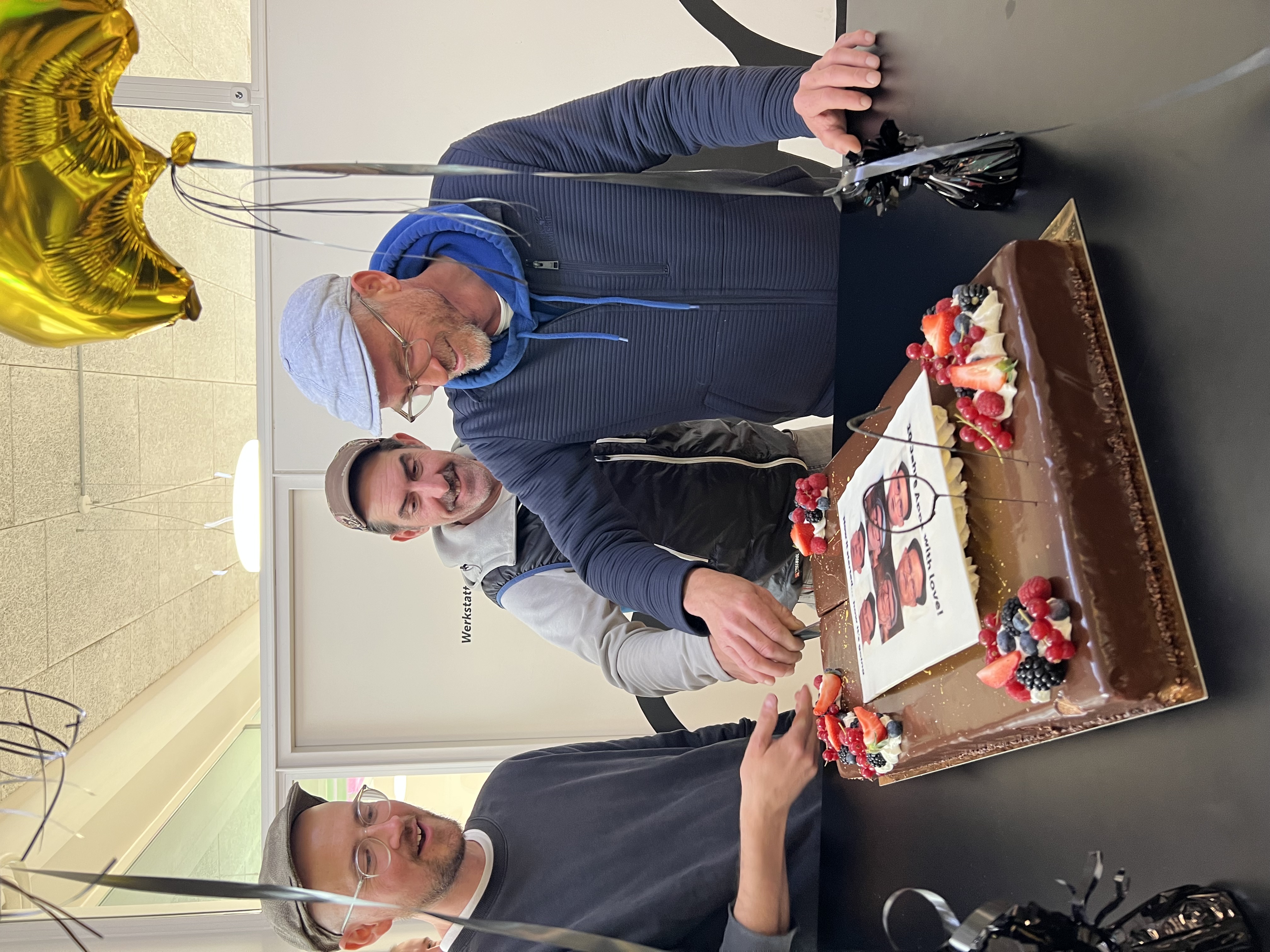 Stefan, Res und Michael schneiden gemeinsam eine Torte an