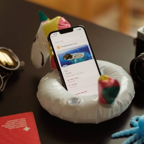 Die Travel Admin App des EDA geöffnet auf einem iPhone, das in einem aufblasbaren kleinen Schwimmring platziert ist