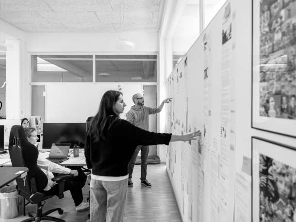 Das Marketing und Sales Team schaut gemeinsam Texte an, die an einer Wand im Büro aufgehängt sind.